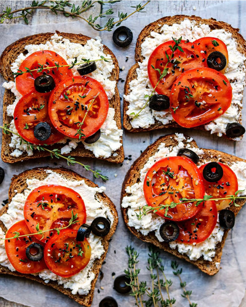 Tomaten-Ricotta-Toast mit Minos BIO Kalamata Oliven, frischen Tomatenscheiben, Ricotta und Thymian, verfeinert mit Minos Natives Olivenöl Extra für Salate.