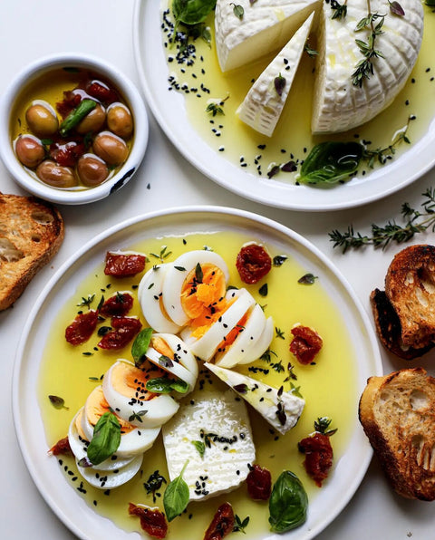 Gesundes mediterranes Frühstück mit hartgekochten Eiern, cremigem Käse, Minos BIO Grünen Oliven mit Paprika und Minos BIO Nativem Olivenöl Extra, serviert mit geröstetem Brot