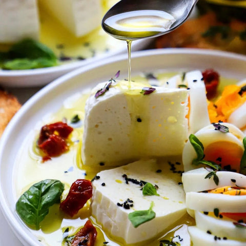 Ein köstliches Gericht mit frischem Feta, verfeinert mit Minos Olivenöl Extra, geschnittenen Eiern und getrockneten Tomaten. Serviert auf einem Teller mit frischen Kräutern, für eine gesunde, mediterrane Mahlzeit.