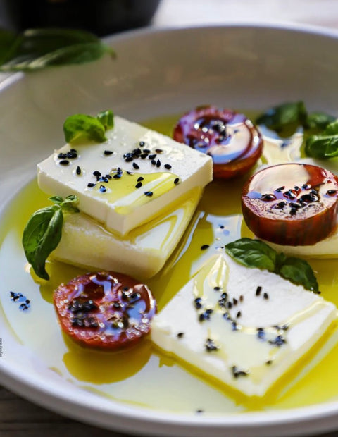 Frischer Feta in hochwertigem Minos Bio-Olivenöl, garniert mit frischen Tomaten, Basilikum und schwarzem Sesam, serviert als mediterrane Vorspeise.