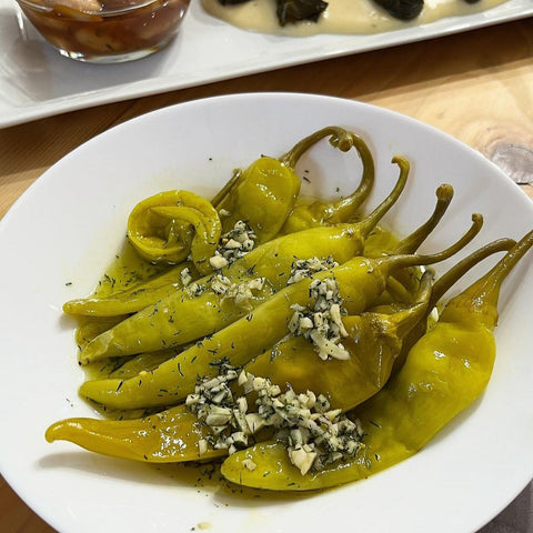 Ein Teller mit Minos Pfefferoni mild-pikant, garniert mit frischem Knoblauch und Dill. Perfekt als Vorspeise oder Beilage für mediterrane Gerichte.